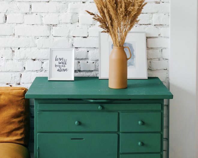 Green dresser with two picture frames and a vase